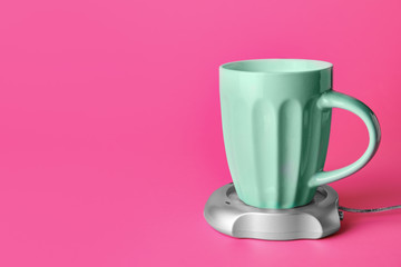 Cup of coffee with heater on color background