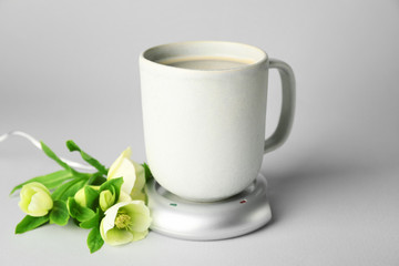 Cup of coffee with heater and flowers on light background