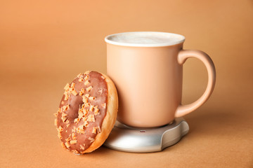 Cup of coffee with heater and donut on color background