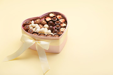Heart-shaped box with chocolate candies on color background
