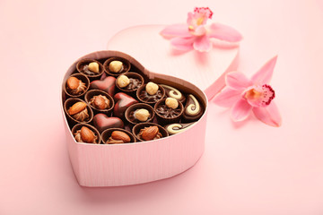 Heart-shaped box with chocolate candies on color background