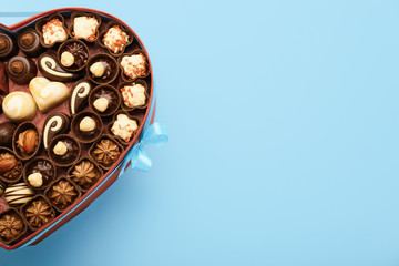 Heart-shaped box with chocolate candies on color background