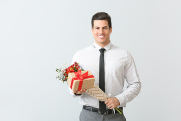 Handsome man with bouquet of flowers and gift on light background