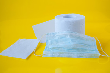 One roll of white toilet paper and a medical mask on a yellow background