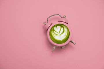green japanese matcha tea in a pink alarm clock on a pastel pink background copy space, detox and...