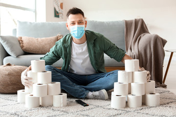 Man in mask and with heap of toilet paper at home. Concept of coronavirus epidemic