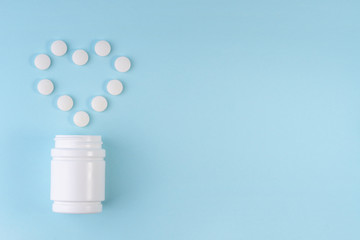 White medical pills spilling out of bottle in heart form on blue. Tablets from heart disease. Medication and heart symbol. Healthcare, health insurance, medicine, concept. Top view, copy space