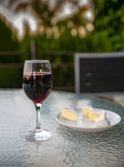 Glass of red wine, plate with cheese on a glass table. Vintage style.