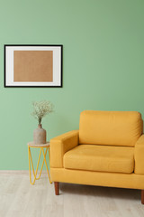Stylish vase with beautiful bouquet on table and armchair near color wall