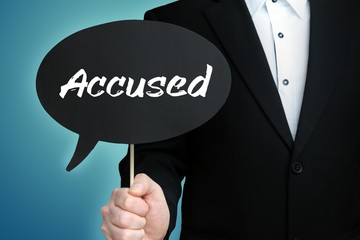 Accused. Lawyer in suit holds speech bubble at camera. The term Accused is in the sign. Symbol for law, justice, judgement