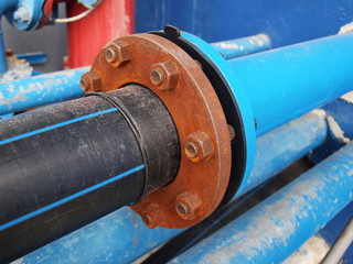 Bolt with old screws at the black plastic water supply pipe connection and blue metal pipe. Selective focus