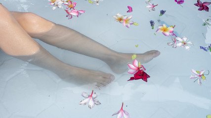 Fototapeta na wymiar Feet soaking in water with flowers in swimming pool. taking care, spa and relaxation. taking holiday concept.