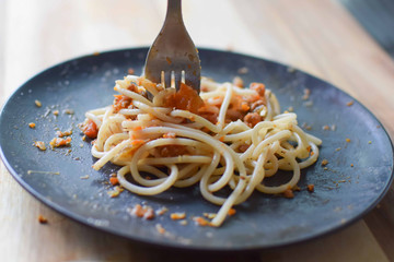 Spaghetti Bolognese on a black pate and a silver fork.
