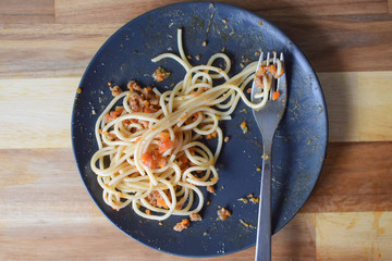 Serving of Spaghetti Bolognese on a black plate with silver and fork. Half ate serving of a spaghetti bolognese on a black plate.