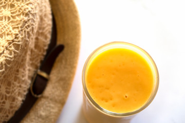 Top view - soft focus of juicy smoothie organic pineapple & orange with sun hat on white table background, Refreshing & healthy drink during hot or warm weather when travel concept, copy free space 