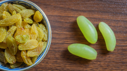 Green raisins kept in a chinaware on a wooden kitchen top along with a bunch of green grapes