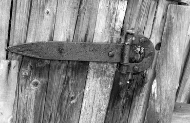 Vintage metal door hinge closeup on old wooden door background. Black and white photography