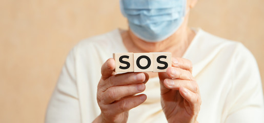 Elderly woman holds wooden cubes in her hands with the inscription SOS. Medical concept