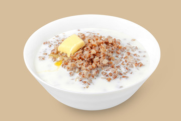 Deep white plate with buckwheat porridge with milk and a melting slice of butter close-up.