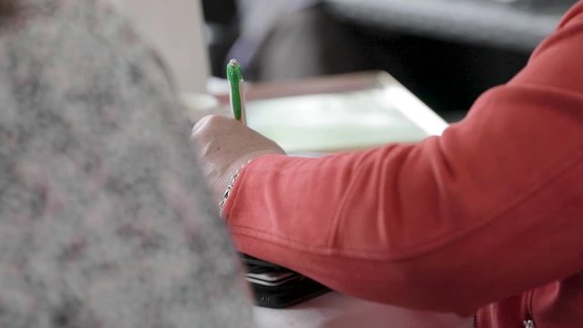 Left-handed woman writing notes on paper with a pen in slow motion.