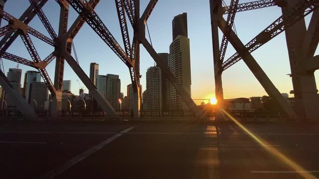 Pan view orange setting sun through buildings from Story Bridge over Brisbane River