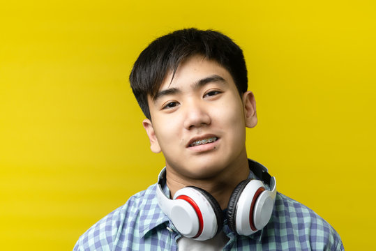 Asian Teenager Using Headphone On Yellow Background.