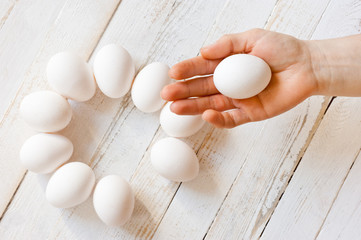A white chicken egg lying in a man’s hand, shot on a white painted wooden surface. Background for livestock products.
