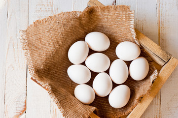 White chicken eggs lying in a canvas bag, shot on a white painted wooden surface. Background for livestock products.