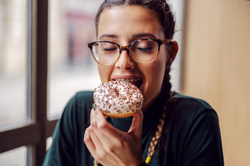 Portrait of young girl sitting in pastry shop and eating doughnut.
