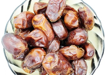 Dried dates in a transparent plate are placed on a white background
