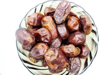 Dried dates in a transparent plate are placed on a white background