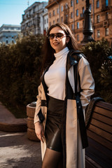Obraz premium Young stylish woman at city. Fashion model girl in trendy coat . Female fashion and lifestyle. In a black and white coat, white sweater, black blouse. In sunglasses