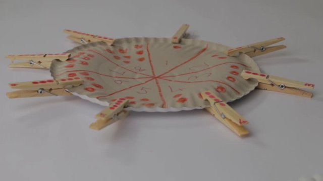Tlit of paper plate with numbers written on it with wooden clothing pegs