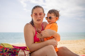 a young Caucasian girl in pink glasses and a bathing suit is holding a child in glasses and a T-shirt in her arms. they are smiling at the camera on the background of sea waves