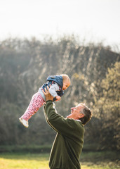 Grandfather proudly rising his granddaugther above his head while enjoying sunny day outdoors.