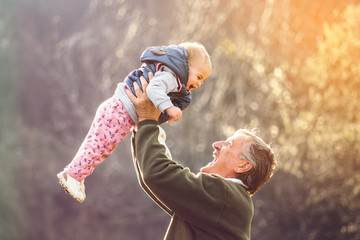 Grandfather proudly rising his granddaugther above his head while enjoying sunny day outdoors.