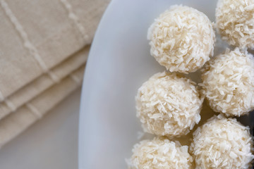 Candies in plate covered by chocolate, shredded coconut and kitchen towel on rustic wooden background.