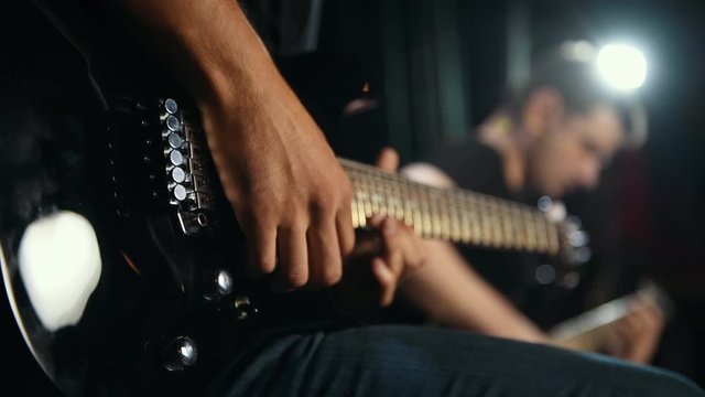 Two male guitarists in black clothes performing song in dark room.