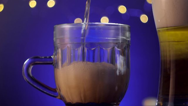 Close up pouring glass of beer on blue background