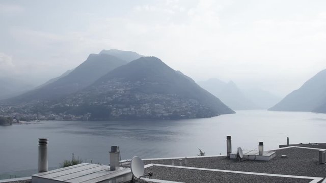 Slow pan over the lake Lugano and the city of Lugano from Paradiso on a cloudy day during summer with monte bre in the background, wider