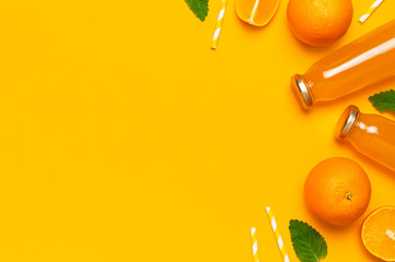 Glass bottles with orange juice, fresh sweet oranges, mint leaves and drinking tubs on yellow background. Healthy food, healthy drink, vitamin C. Creative summer concept. Flat lay top view copy space