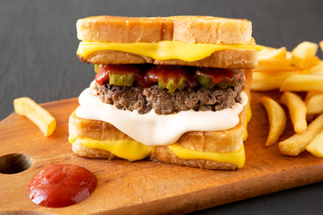 Homemade Grilled Cheese Burger with French Fries on a rustic wooden board on a black background, side view. Close-up.