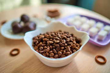 A white plate with a handful of coffee beans is standing on the table. Selective focus