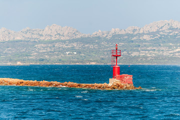 A view of a nautical buoy positioned at the entrance to the port on a sunny day with the coast of the island in the background, in Sardinia Italy

