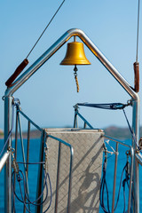 A vertical closeup of the bell on the stern of the ship with in the background the blue sea the coast and the blue sky on a sunny summer day, in Sardinia Italy
