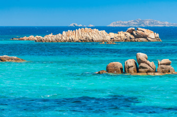 A wonderful view to discover a pristine and colorful sea with the background of granite rocks and some islands on a sunny day in summer, in Sardinia Italy