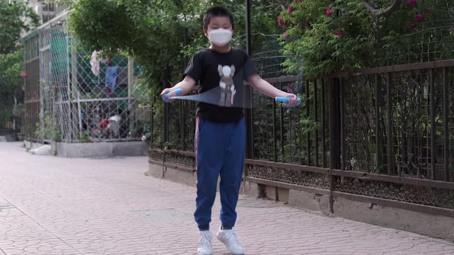 Chinese kid with face mask jumping rope outdoor in corona virus pandemic.
