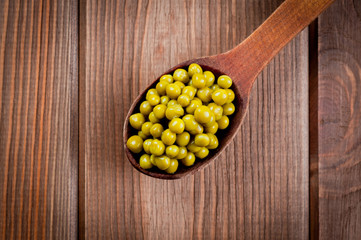 Canned green peas in a wooden spoon lying on a wooden surface of the table.
