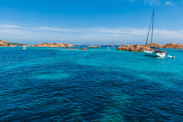 A view of a sailing boat moored in a wonderful and colorful bay of the Mediterranean sea with some rocks in the background on a sunny day with some clouds in summer, in Sardinia Italy
