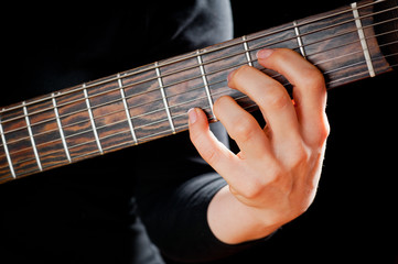 Seven-string electric guitar made of dark wood and human hands, shot on a dark background....